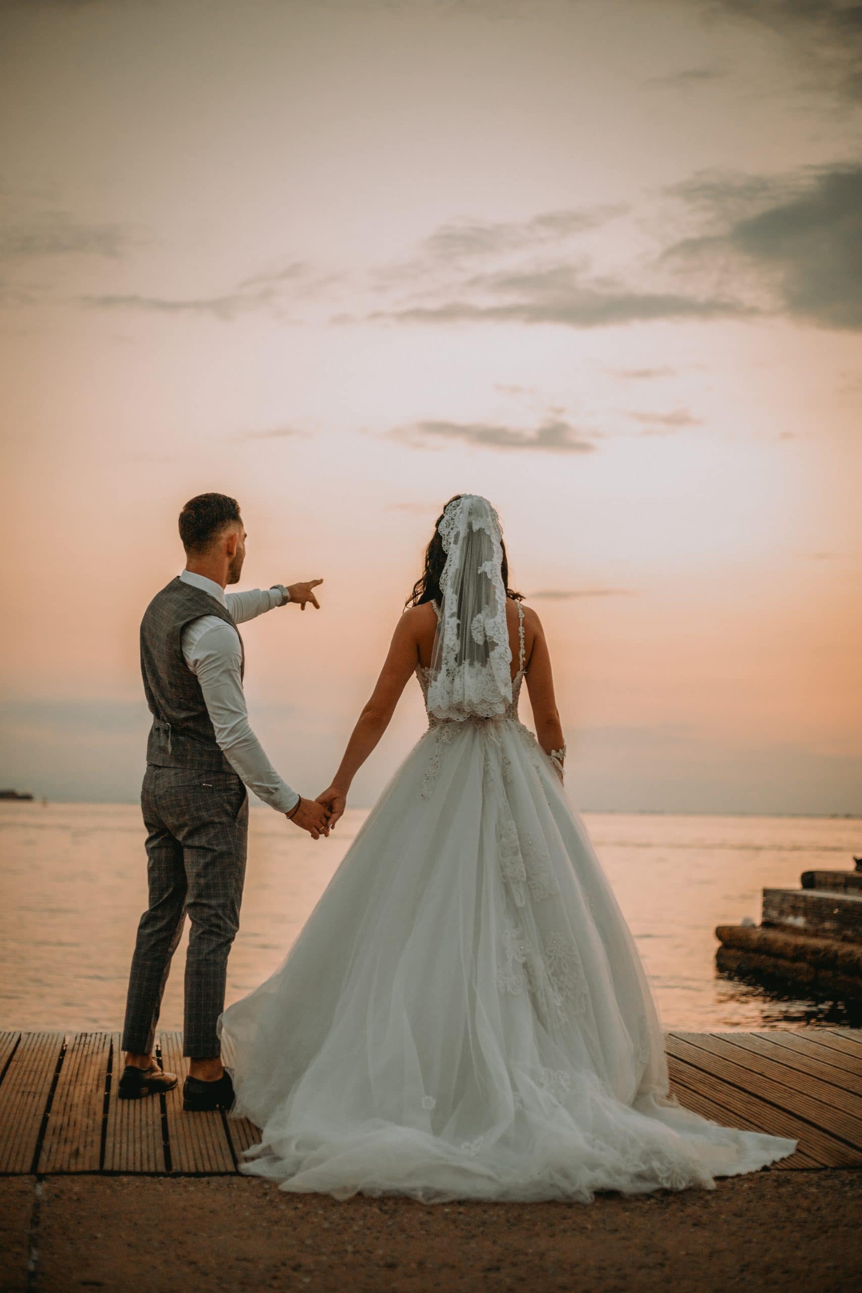 Φωτογραφία που ένα ζευγάρι αγναντεύει στον ορίζοντα και κάνει όνειρα και βλέψεις για το μέλλον.Ο γαμπρός φοράει γκρι κοστούμι και η νύφη ενα λευκό νυφικό με πέπλο η λήψη έγινε απο τον φωτογράφο γάμου Καρασαββίδη Γιώργο στην Νέα Παραλία Θεσσαλονίκης την ώρα του ηλιοβασιλέματος σε μια ρομαντική ατμόσφαιρα